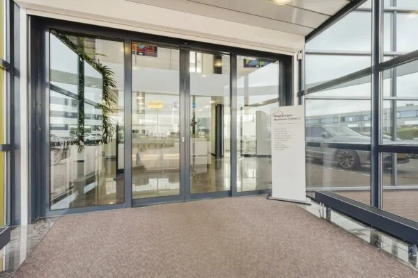 Ingang van Regenbogen Business Center 1 aan de Laan van 's-Gravenmade met glazen schuifdeuren en een informatief welkomstbord.